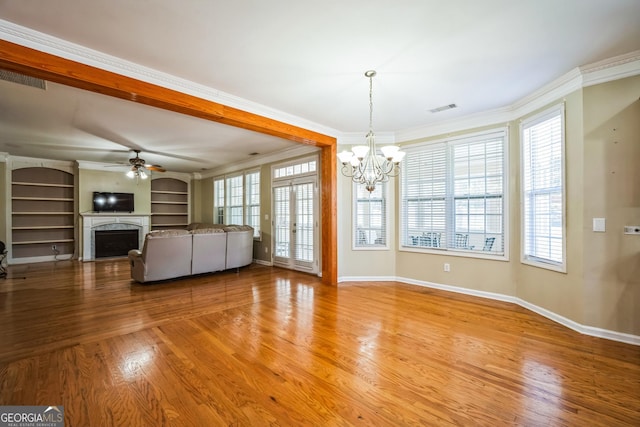 unfurnished living room featuring visible vents, a fireplace, ornamental molding, wood finished floors, and ceiling fan with notable chandelier