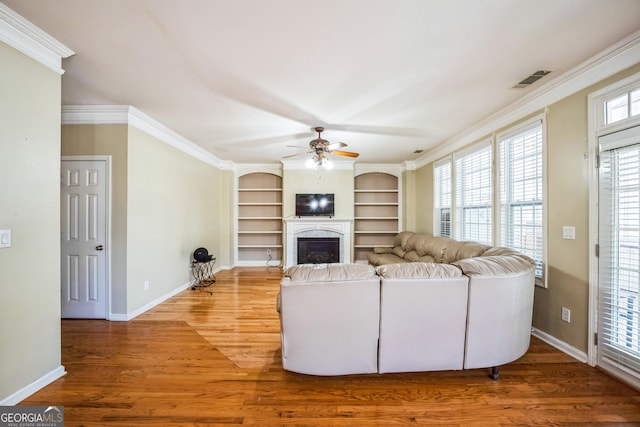 living area with a fireplace, wood finished floors, a healthy amount of sunlight, and a ceiling fan