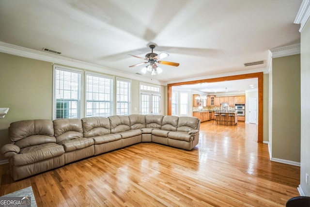 living room with light wood-style flooring, ornamental molding, visible vents, and a ceiling fan