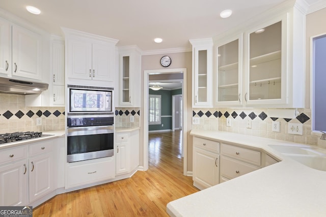 kitchen with ornamental molding, appliances with stainless steel finishes, under cabinet range hood, light countertops, and a sink