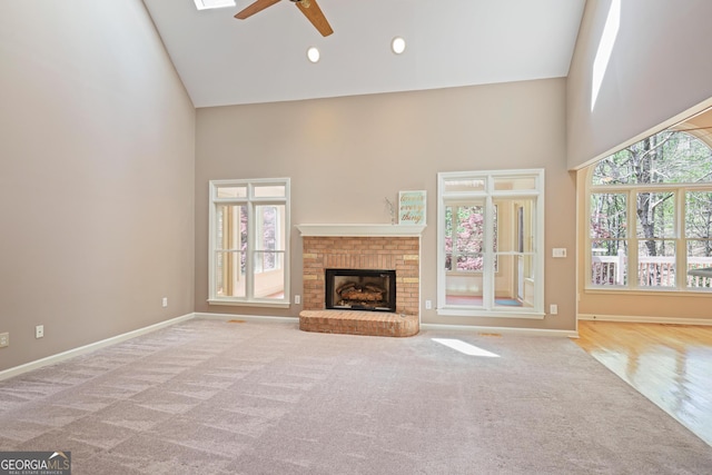 unfurnished living room with high vaulted ceiling, a ceiling fan, carpet floors, a brick fireplace, and baseboards