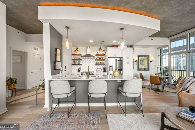 kitchen featuring wall chimney range hood, a breakfast bar area, decorative backsplash, light countertops, and stainless steel fridge