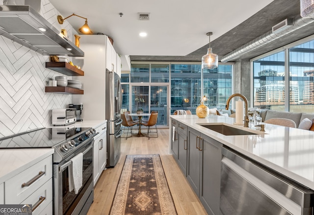 kitchen featuring open shelves, light wood-style flooring, a sink, appliances with stainless steel finishes, and range hood