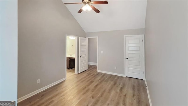 unfurnished bedroom featuring baseboards, ensuite bathroom, light wood-style flooring, and high vaulted ceiling
