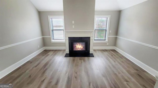unfurnished living room with baseboards, a glass covered fireplace, wood finished floors, and lofted ceiling