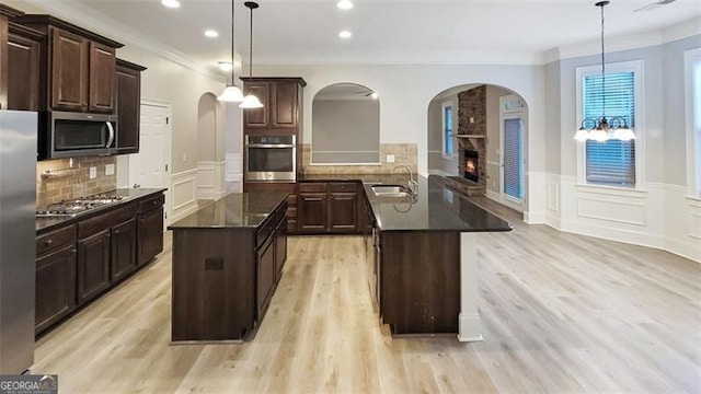 kitchen with a kitchen island with sink, appliances with stainless steel finishes, arched walkways, a sink, and a decorative wall