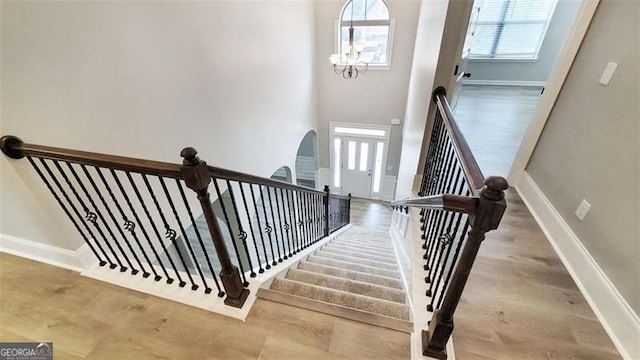 staircase with baseboards, arched walkways, wood finished floors, and a notable chandelier