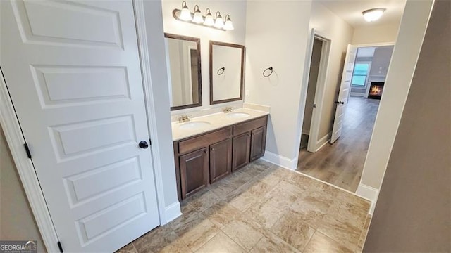 bathroom with double vanity, a sink, baseboards, and a warm lit fireplace