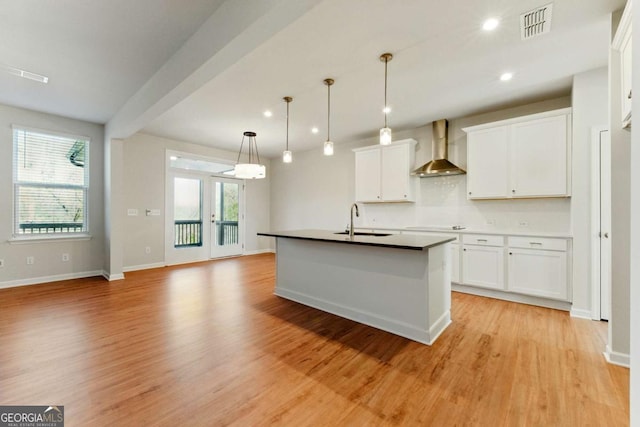 kitchen with visible vents, light wood-style flooring, wall chimney exhaust hood, white cabinetry, and a sink