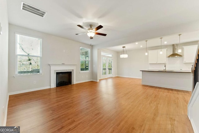 unfurnished living room with light wood-style flooring, visible vents, a fireplace, a ceiling fan, and a sink