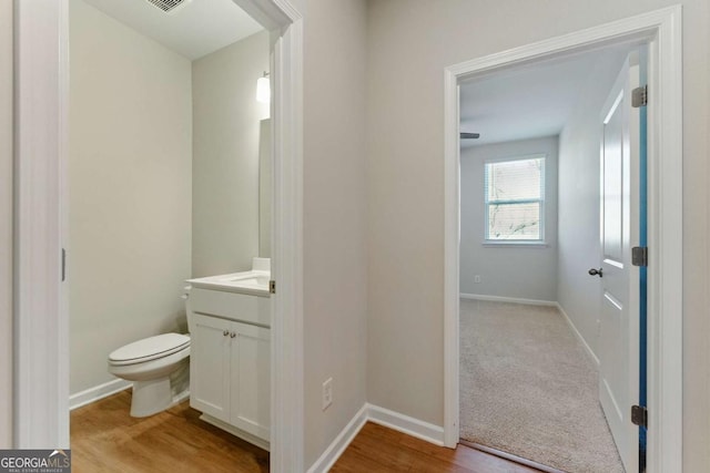 bathroom with vanity, toilet, baseboards, visible vents, and wood finished floors