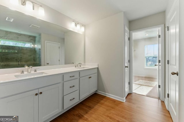 full bathroom featuring a shower stall, double vanity, wood finished floors, and a sink
