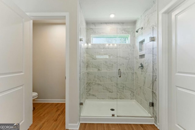 bathroom with toilet, a stall shower, baseboards, and wood finished floors