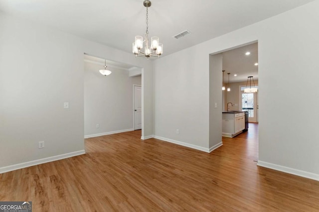 unfurnished dining area featuring baseboards, a sink, visible vents, a notable chandelier, and wood finished floors