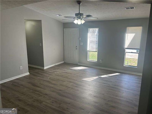 interior space featuring a textured ceiling, visible vents, baseboards, a ceiling fan, and dark wood finished floors