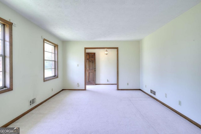 unfurnished room with a textured ceiling, baseboards, light colored carpet, and visible vents