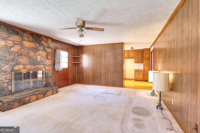 unfurnished living room featuring a textured ceiling, wooden walls, a ceiling fan, and light carpet