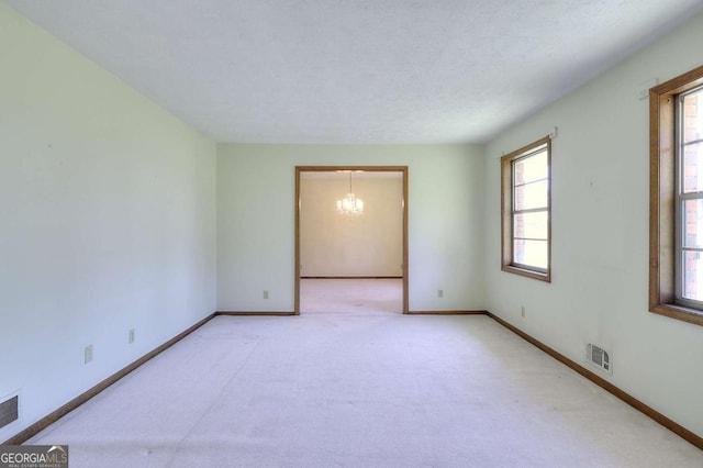 empty room featuring a textured ceiling, visible vents, baseboards, an inviting chandelier, and light colored carpet
