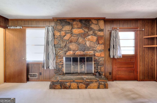 unfurnished living room featuring carpet floors, a stone fireplace, wood walls, and a textured ceiling