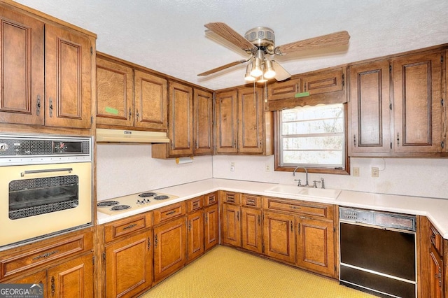 kitchen featuring white appliances, under cabinet range hood, a sink, ceiling fan, and brown cabinetry