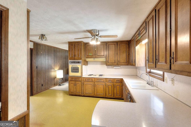 kitchen featuring light countertops, a sink, brown cabinets, white appliances, and ceiling fan