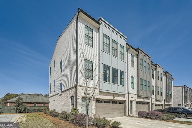 exterior space featuring an attached garage, concrete driveway, a residential view, and brick siding