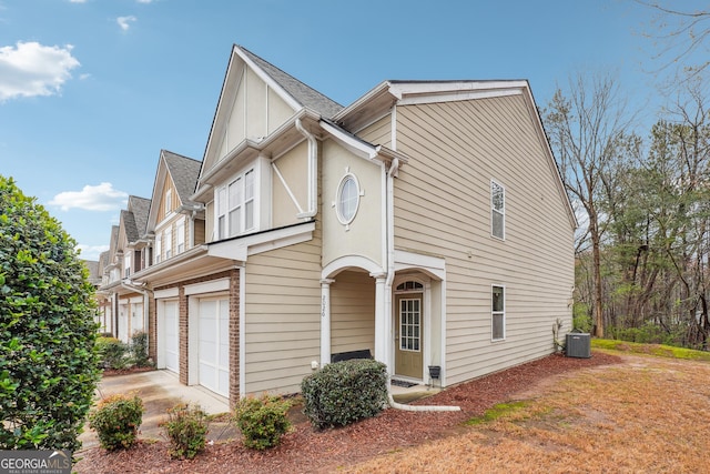 view of front of house featuring central AC unit, an attached garage, and roof with shingles