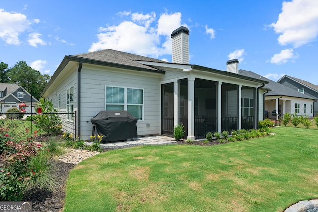 back of house featuring a sunroom, fence, a chimney, a lawn, and a patio area