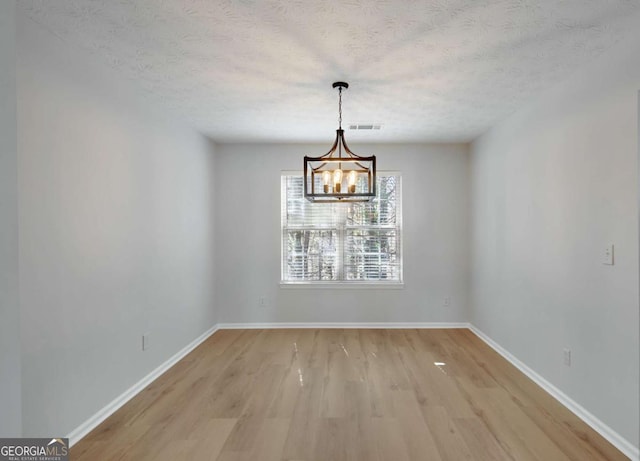 unfurnished dining area with a textured ceiling, visible vents, light wood-type flooring, and an inviting chandelier
