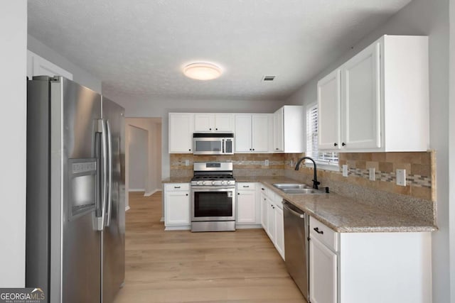 kitchen featuring decorative backsplash, white cabinets, visible vents, stainless steel appliances, and a sink