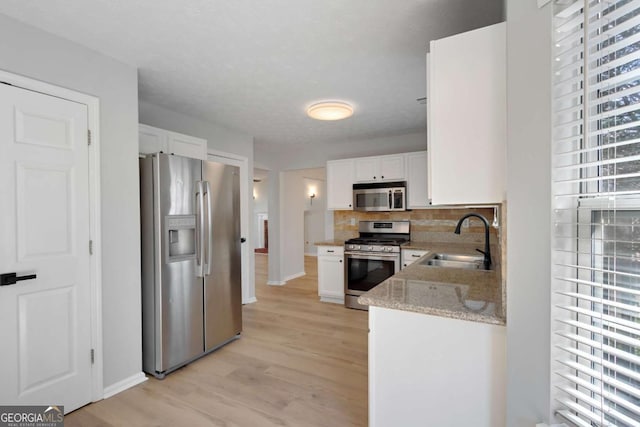 kitchen featuring white cabinetry, stainless steel appliances, decorative backsplash, a sink, and light wood finished floors