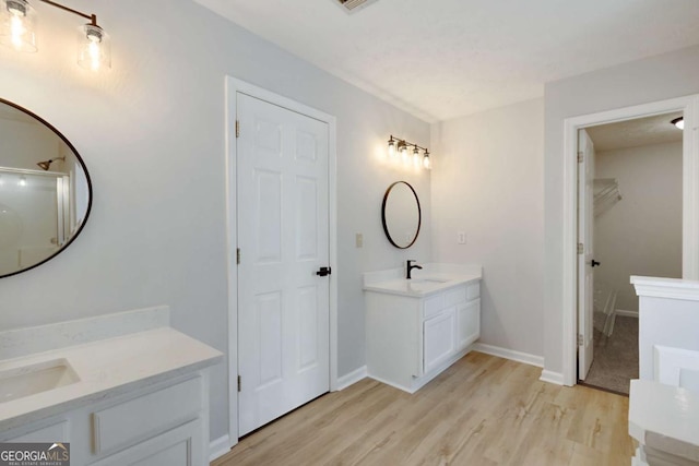 full bathroom with a sink, two vanities, wood finished floors, a walk in closet, and baseboards