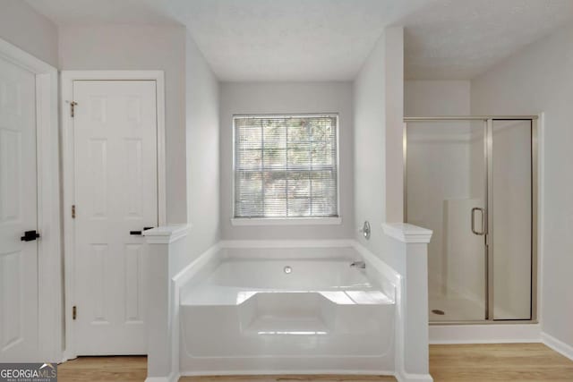 full bathroom with a bath, a textured ceiling, wood finished floors, and a stall shower