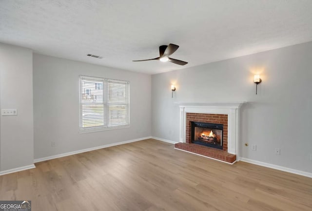 unfurnished living room with a brick fireplace, visible vents, light wood-style floors, and a ceiling fan