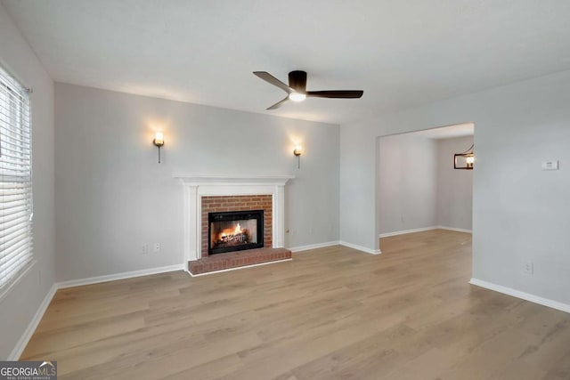 unfurnished living room with a brick fireplace, baseboards, light wood-style floors, and ceiling fan