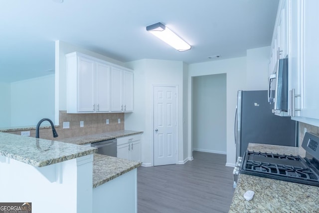 kitchen with white cabinets, a peninsula, light stone countertops, stainless steel appliances, and backsplash