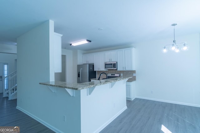 kitchen with white cabinetry, a breakfast bar, backsplash, light stone countertops, and appliances with stainless steel finishes