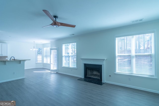 unfurnished living room featuring a fireplace, dark wood-style floors, baseboards, ceiling fan with notable chandelier, and visible vents