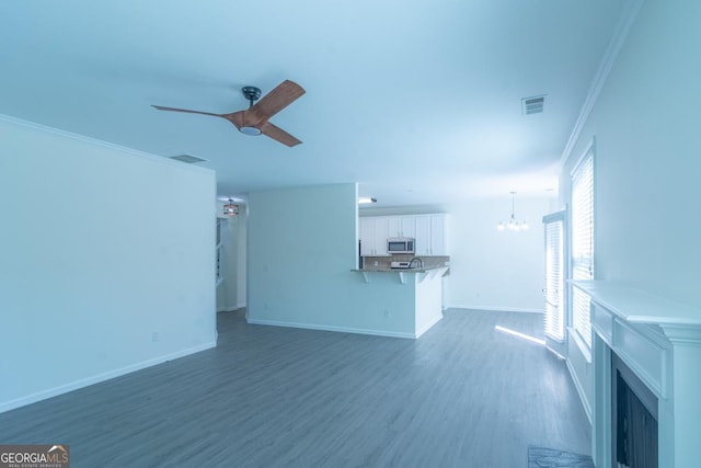 unfurnished living room featuring visible vents, baseboards, ornamental molding, dark wood-type flooring, and ceiling fan with notable chandelier
