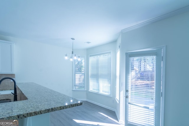 kitchen with white cabinets, light stone countertops, a sink, hanging light fixtures, and an inviting chandelier