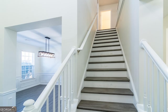 staircase with a decorative wall, wood finished floors, and wainscoting