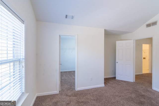 unfurnished bedroom with a spacious closet, carpet floors, vaulted ceiling, and visible vents