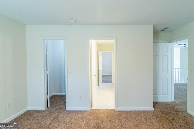 unfurnished bedroom with baseboards, carpet floors, visible vents, and a walk in closet