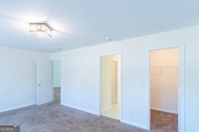 unfurnished bedroom with a closet, a walk in closet, carpet, and baseboards