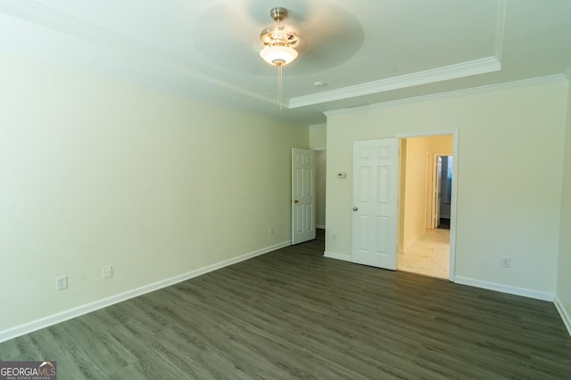 unfurnished bedroom featuring a tray ceiling, ornamental molding, and dark wood finished floors