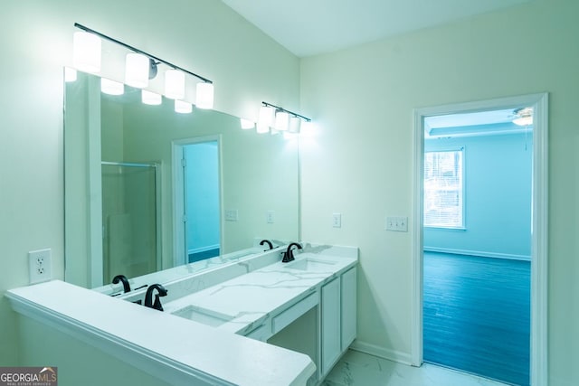 bathroom featuring marble finish floor, a shower with shower door, baseboards, and a sink