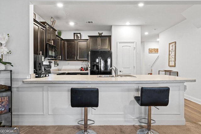 kitchen featuring light countertops, black appliances, dark brown cabinets, and a kitchen breakfast bar