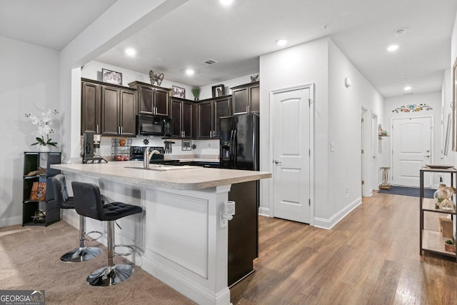 kitchen with light countertops, a sink, a peninsula, black appliances, and dark brown cabinets