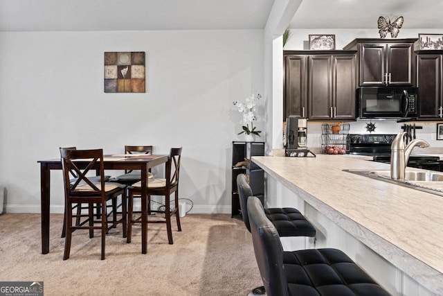 kitchen with light countertops, a kitchen bar, baseboards, light colored carpet, and black appliances