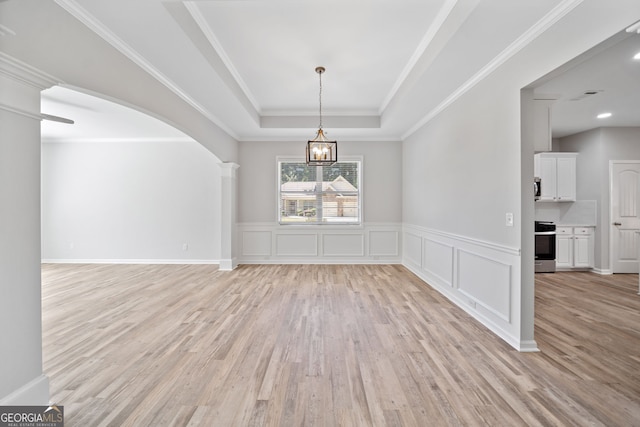 unfurnished dining area featuring a tray ceiling, a wainscoted wall, light wood-style floors, and a chandelier